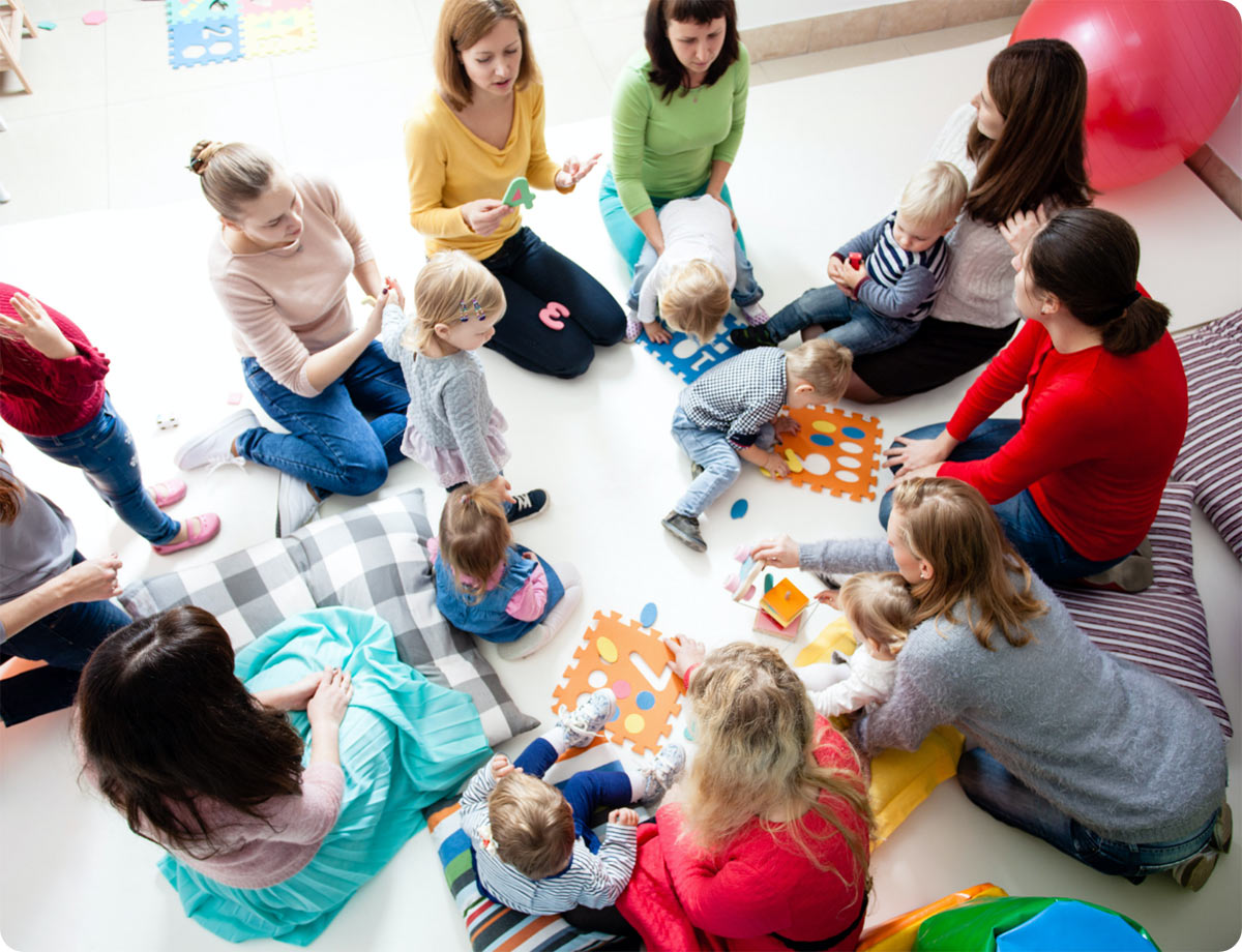 an image of a group of mothers sitting in a circle with their baby listening to a woman who is showing them all something