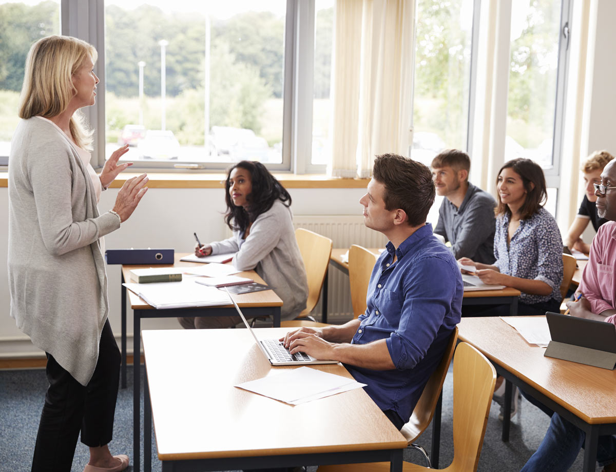 a health care professional leading a class with students sitting with their laptops in front of them